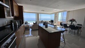 Una cocina moderna con una isla grande, un comedor con vista al océano y una sala de estar espaciosa con un ventanal con vistas al mar.