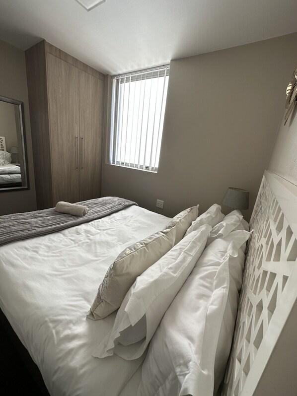 Un dormitorio con cama, ventana con persianas, espejo y armario.