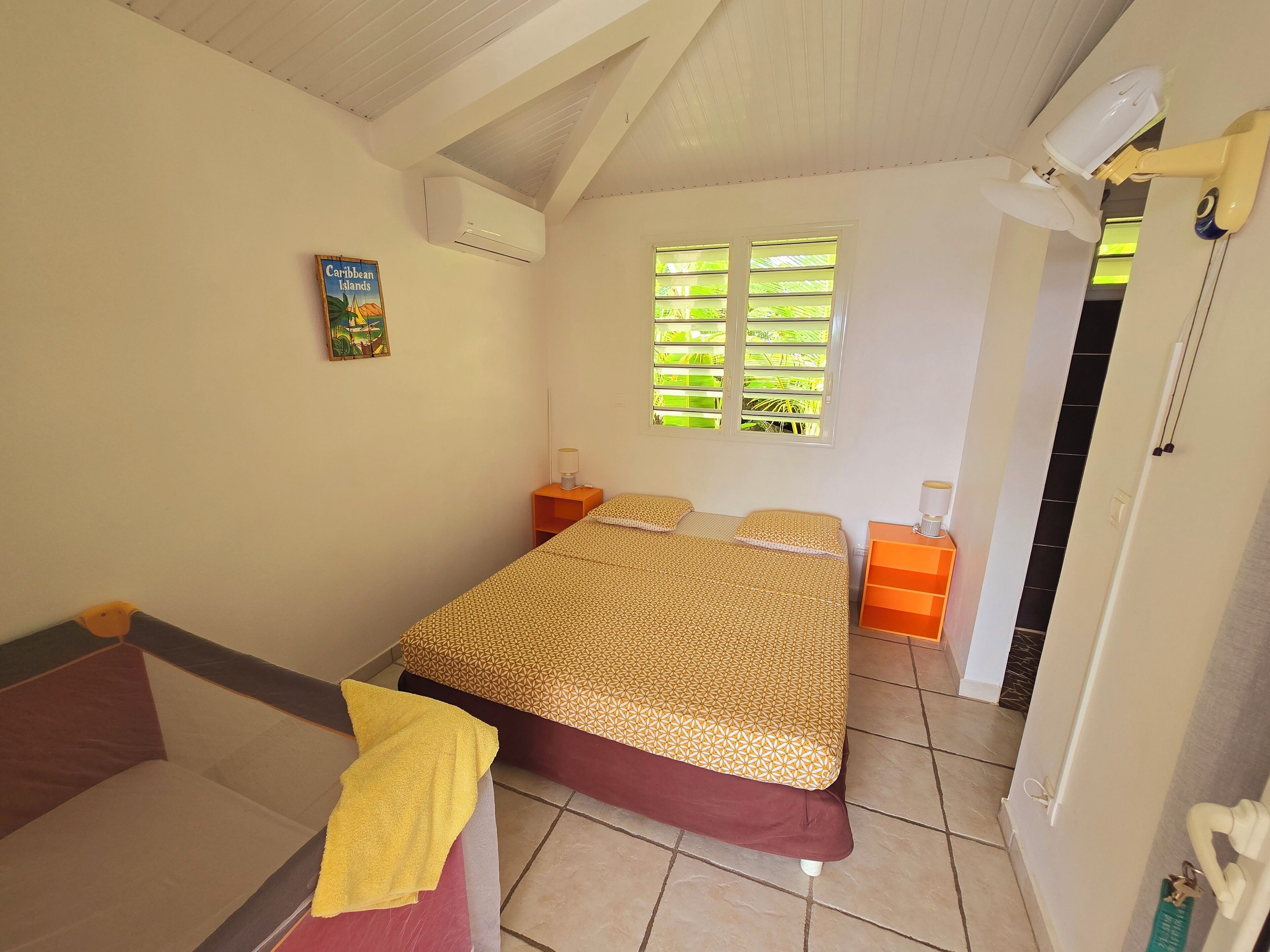 A bedroom with a bed, a nightstand, a lamp, a window with blinds, and a door.