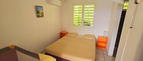 A bedroom with a bed, a nightstand, a lamp, a window with blinds, and a door.