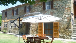 A stone building with a patio table and chairs under a white umbrella. - ancient villa with pool and park in total privacy (tuoro sul trasimeno)