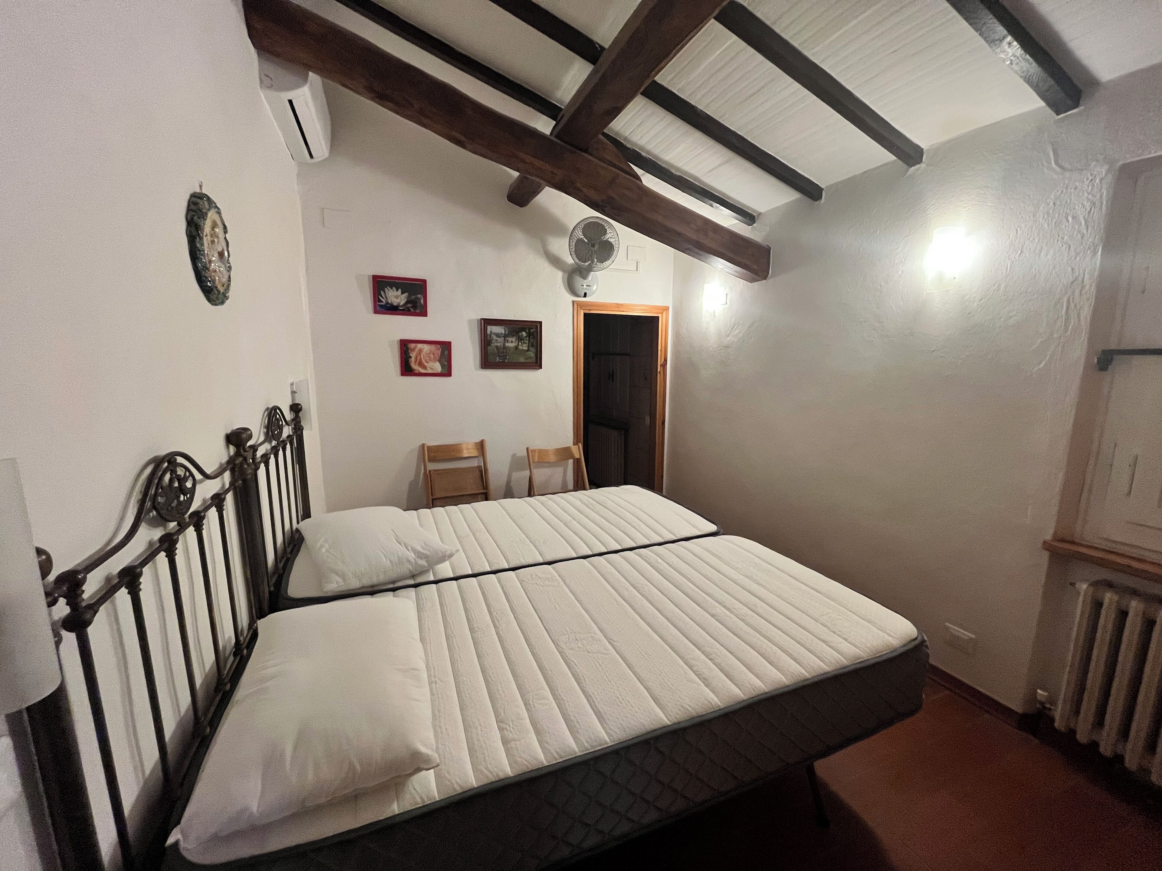 Een slaapkamer met een bed, houten hoofdbord, twee stoelen, een radiator en een deur.