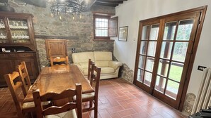 A dining area with a wooden table and chairs, a stone wall, and a window with a view of greenery. - ancient villa with pool and park in total privacy (tuoro sul trasimeno)