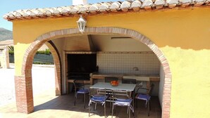 Een buitenkeuken met een bakstenen boog, een betegelde spatwand en een tafel met stoelen.