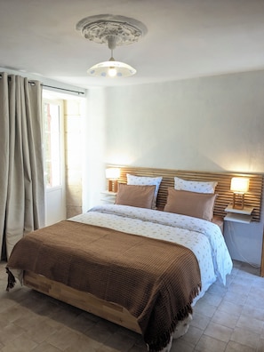 A bedroom with a bed, curtains, a nightstand with a lamp, a ceiling light fixture, and a window.