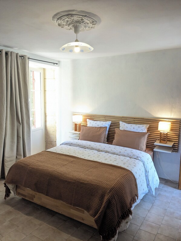 A bedroom with a bed, curtains, a nightstand with a lamp, a ceiling light fixture, and a window.