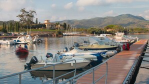 A marina with boats docked along a wooden pier, surrounded by hills and a building in the background. - Villa Giolù, Appartamento Corallo 200 m from the sea, ferry discount! (Portoferraio)