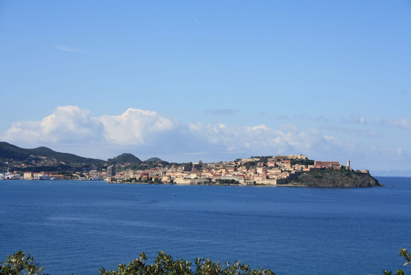 A coastal town with buildings on a hillside and a lighthouse on a small island.