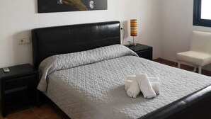 Quarto com cama, mesa de cabeceira, luminária, cadeira e janela.