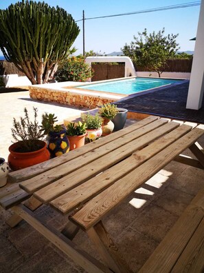 A wooden bench in a sunny outdoor area with a pool, surrounded by potted plants and a stone wall. - Beautiful Villa with swimming pool in Ibiza town. (Eivissa)