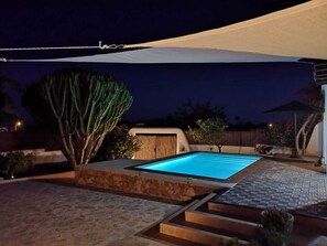 An outdoor swimming pool area with a stone deck, a covered seating area, and a large tree. - Beautiful Villa with swimming pool in Ibiza town. (Eivissa)