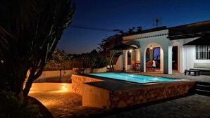 Uma área de piscina com paredes de pedra, um pátio e um espaço coberto com mesas e cadeiras.