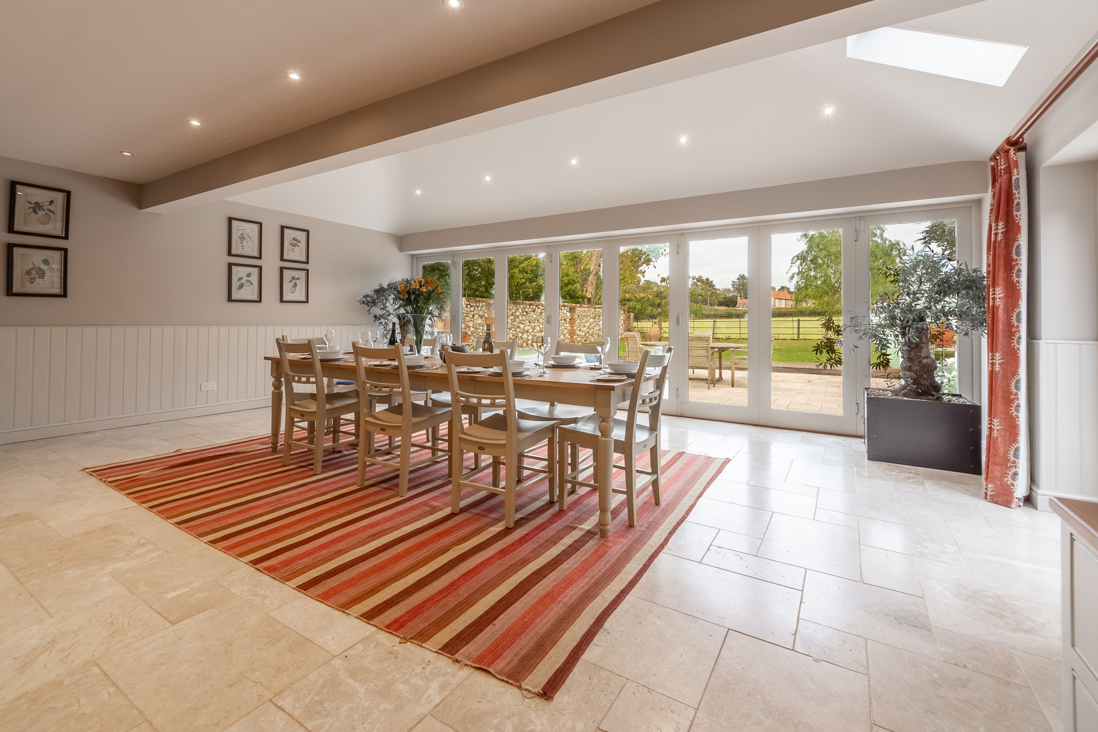 A spacious dining area with a large table and chairs, a striped rug, and a view of the outdoors through large glass doors.