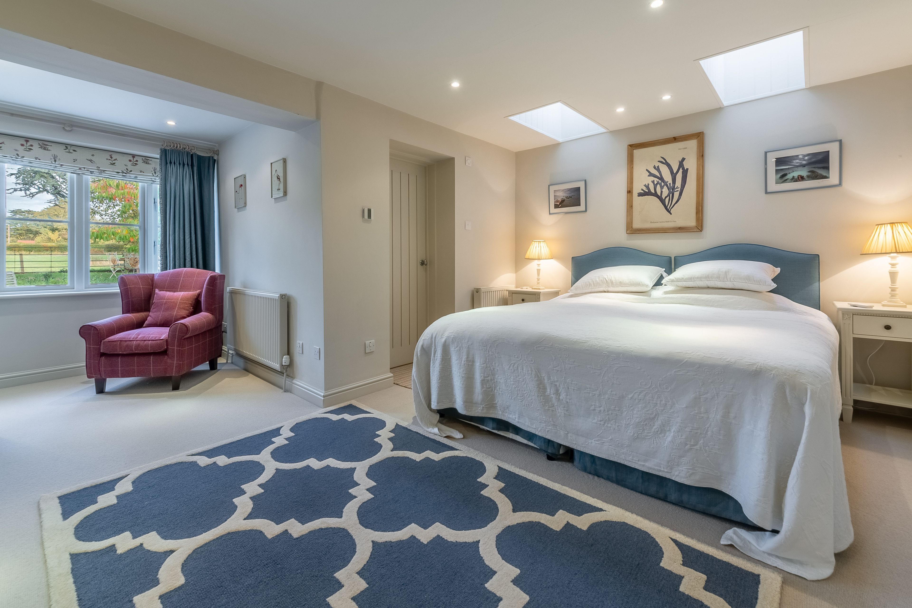 A bedroom with a large bed, a chair, a window with curtains, and a skylight.