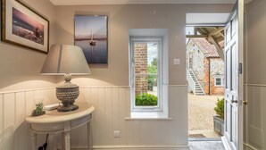 A hallway with a lamp, a framed picture, and a window leading to a brick exterior. - The Little House, Brancaster, Norfolk (Brancaster)