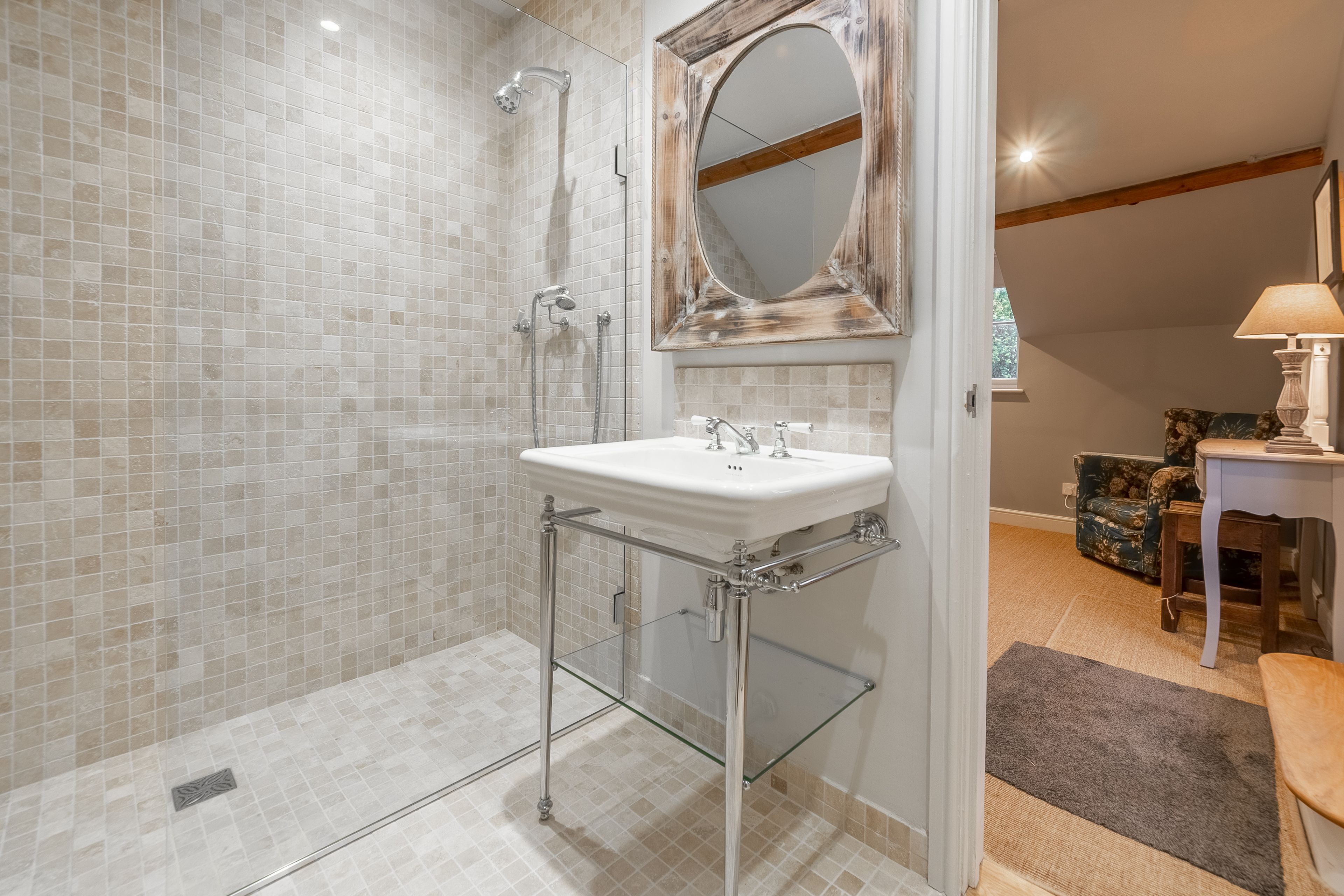 A bathroom with a glass shower enclosure, a white sink with chrome fixtures, and a mirror with a distressed frame.