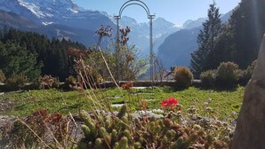 Eine bergige Landschaft mit einer metallenen Bogenstruktur im Vordergrund, umgeben von viel Grün und einem klaren Himmel.