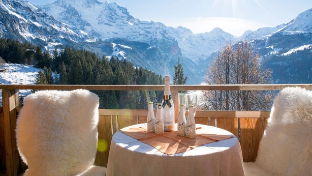 Ein Balkon mit Tisch für zwei Personen, mit Blick auf eine verschneite Berglandschaft.