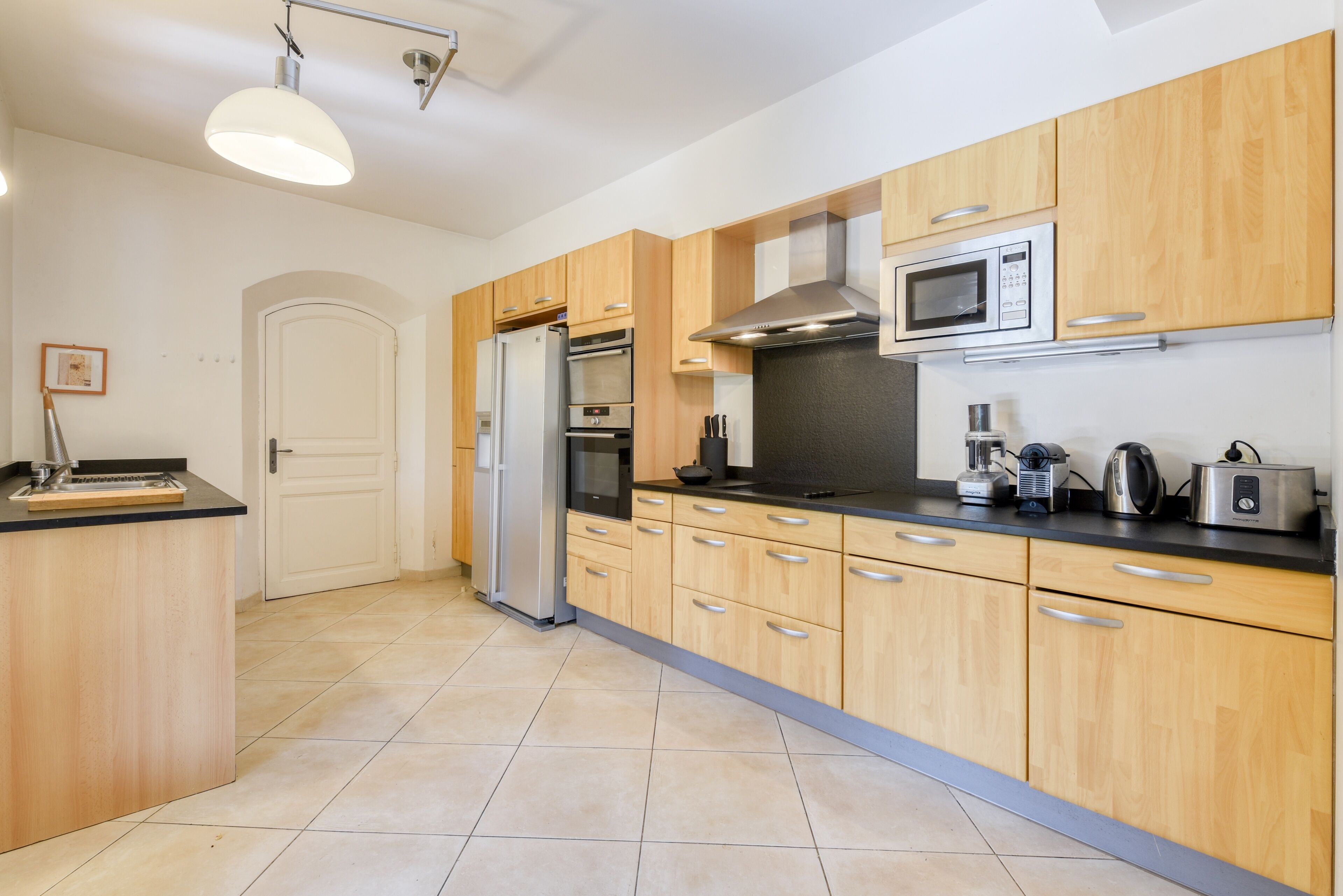 A modern kitchen with wooden cabinets, a stainless steel refrigerator, an oven, a microwave, and a coffee maker.