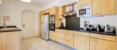 A modern kitchen with wooden cabinets, a stainless steel refrigerator, an oven, a microwave, and a coffee maker.