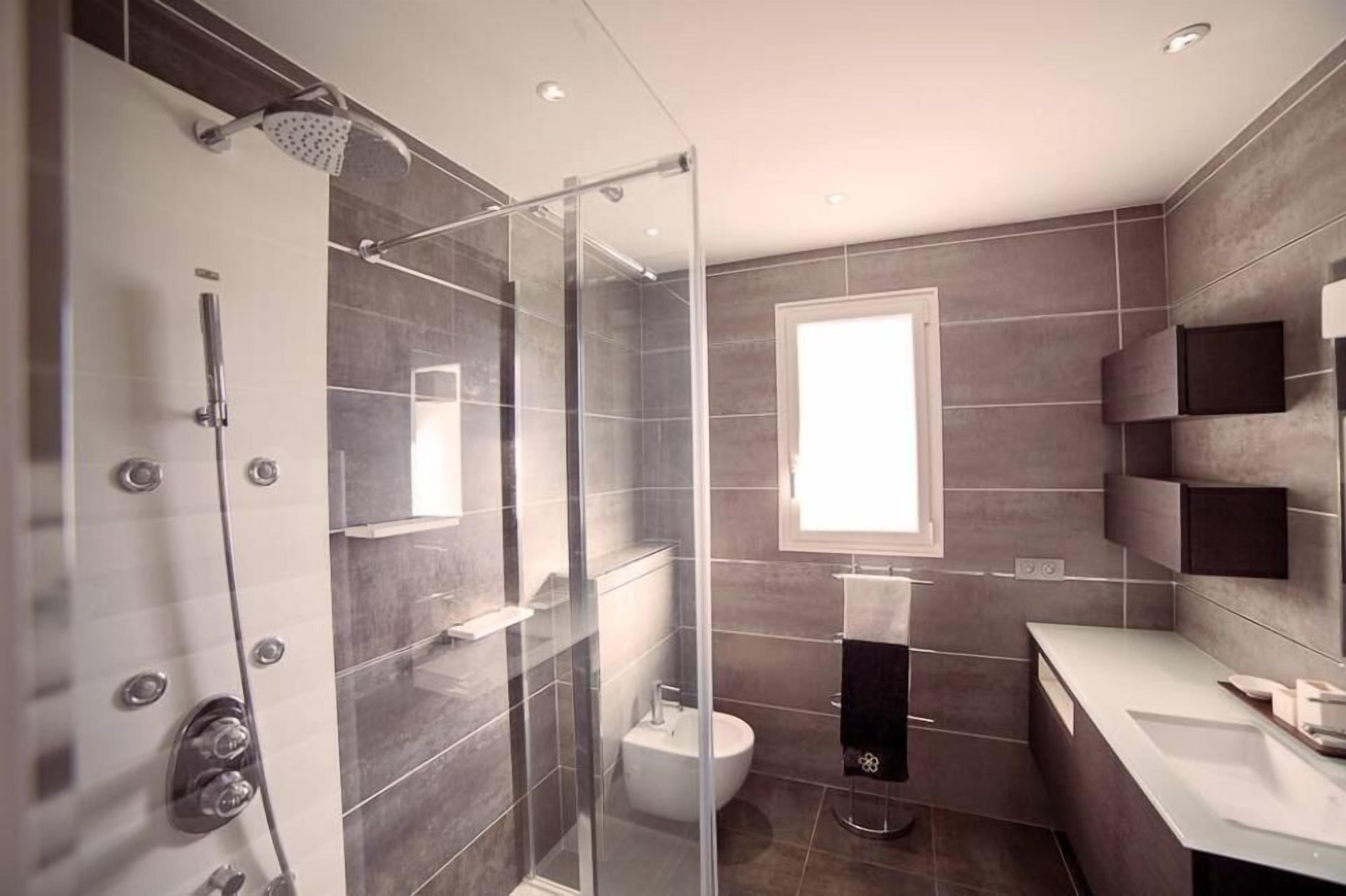 A modern bathroom with a glass-enclosed shower, a toilet, and a sink area.