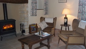 Un salon chaleureux avec une cheminée en pierre, des rideaux à motifs floraux, une table en bois et deux fauteuils.