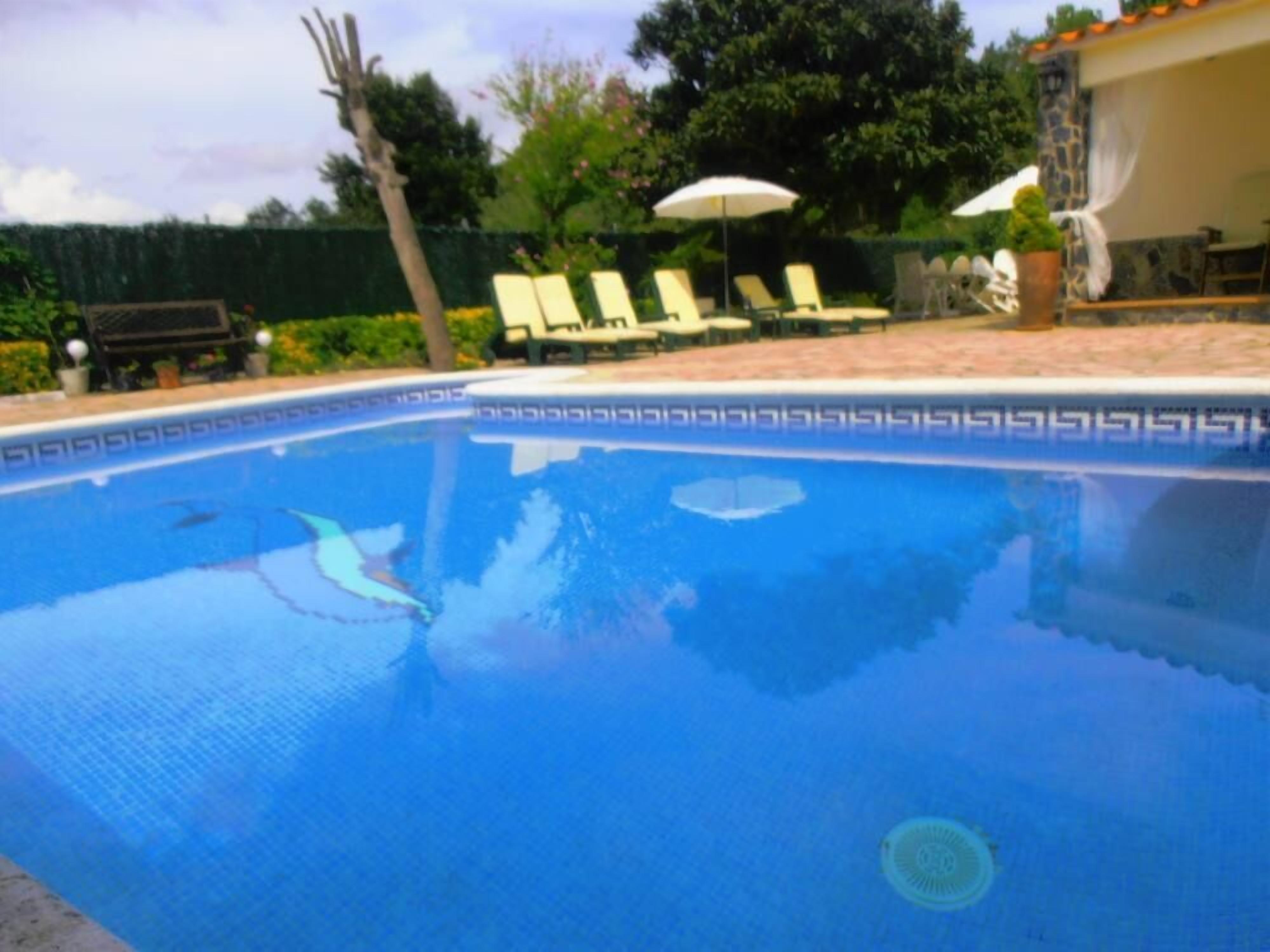 A swimming pool with a tiled edge, surrounded by lounge chairs and umbrellas.