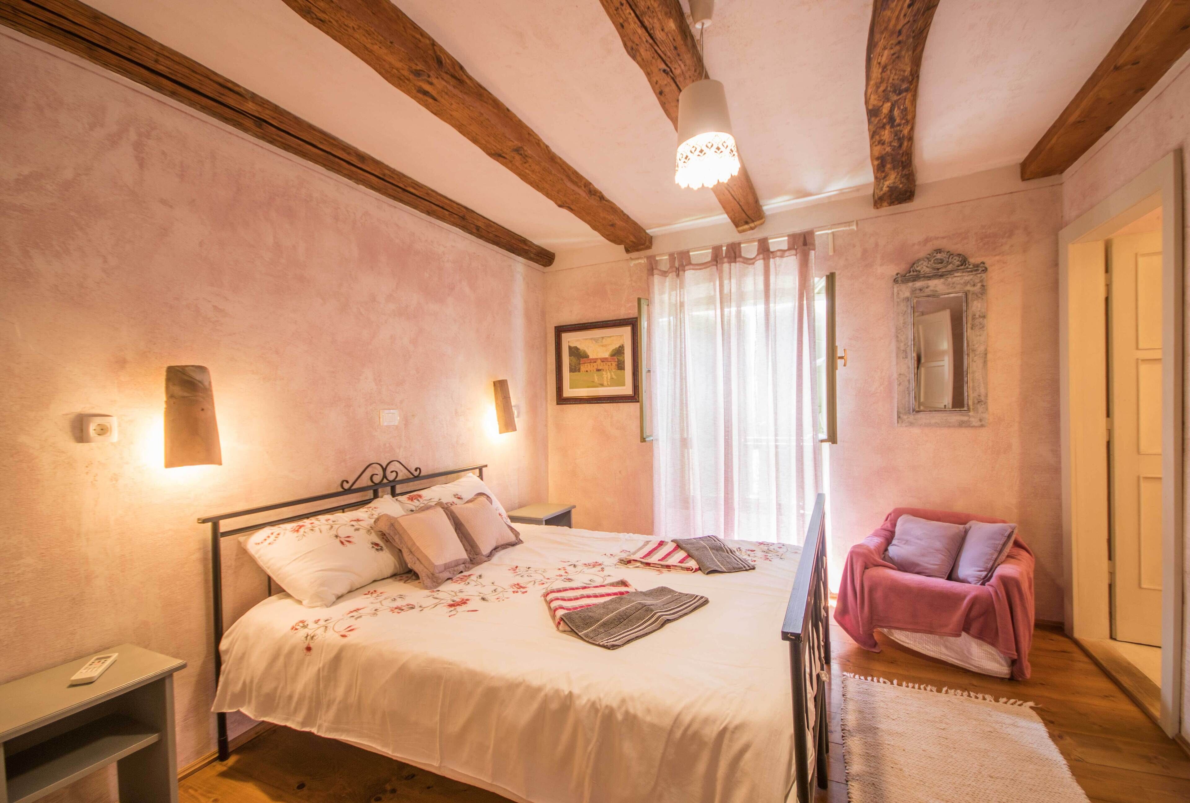 Een slaapkamer met een groot bed, nachtkastjes, een stoel en een raam met gordijnen.