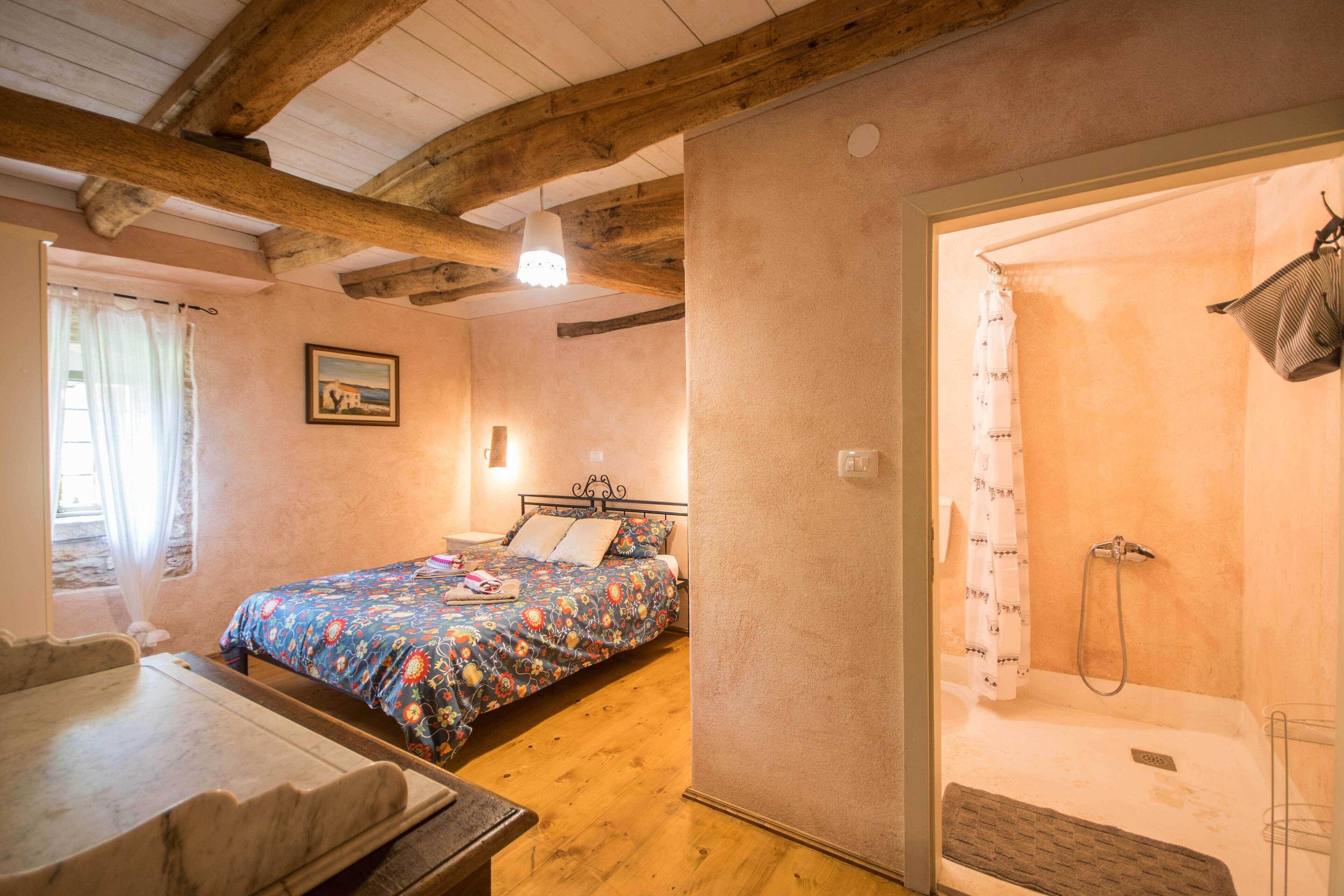 Une chambre à coucher avec un lit, un plancher en bois, un espace douche et une fenêtre avec des rideaux.