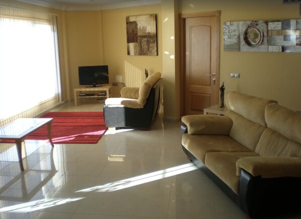 Una sala de estar con un sofá, un sillón reclinable, un televisor y una alfombra roja.