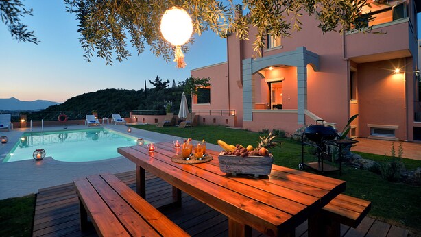 A poolside area with a wooden table, fruit bowl, and outdoor lighting. - Villa Amaryllis is the ultimate booking option for couples, families and friends (Corfu)