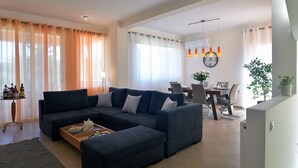 A modern living room with a dark-colored sofa, a coffee table, and a dining area with a table and chairs. - Villa Amaryllis is the ultimate booking option for couples, families and friends (Corfu)
