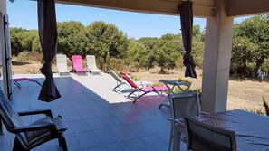 A covered outdoor seating area with lounge chairs and a table, overlooking a garden with trees and a clear sky. - VILLA, 200 m from Bodri BEACH, close to sea view, air-conditioning, large landscaped PARK, (Corbara)
