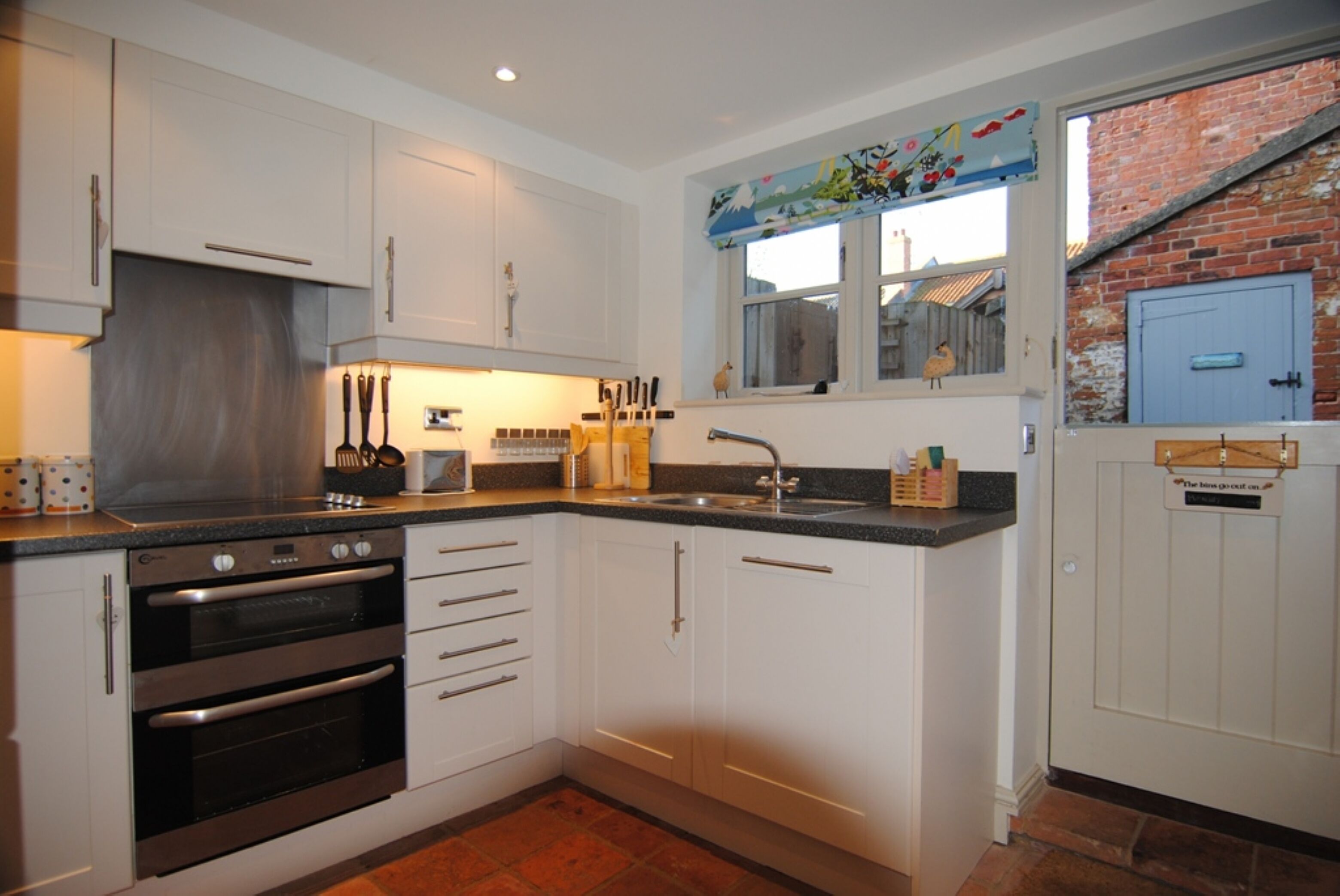 A kitchen with white cabinets, stainless steel appliances, and a window with a view of a brick wall.