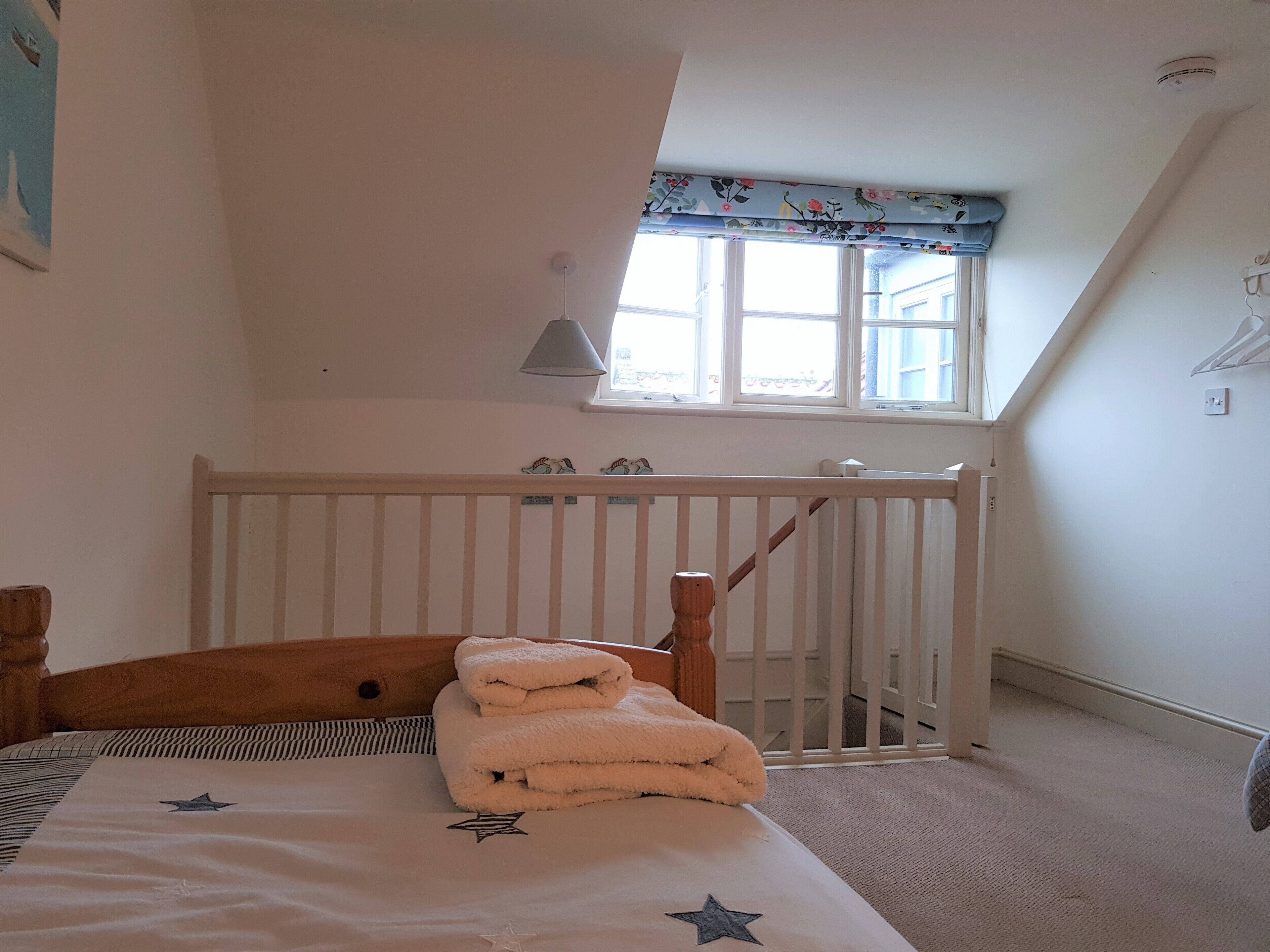A bedroom with a sloped ceiling, a window with a floral valance, a white crib, and a bed with a star-patterned bedspread.