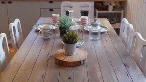 Een houten eettafel met stoelen, een potplant en een raam met uitzicht op bloemen.
