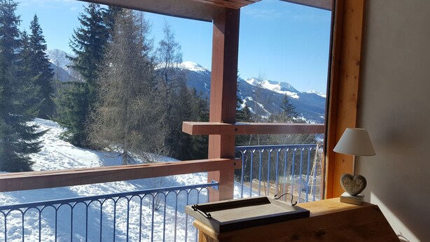 Un balcon en bois offrant une vue sur des montagnes et des arbres couverts de neige.
