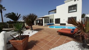 A modern house with a swimming pool, outdoor seating, and potted plants. - Tranquil setting, sea view, heated pool & Hot Tub, sub-tropical garden. (Playa Blanca)