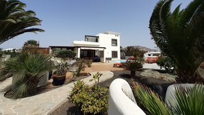 A modern two-story house with a pool, surrounded by palm trees and potted plants. - Tranquil setting, sea view, heated pool & Hot Tub, sub-tropical garden. (Playa Blanca)