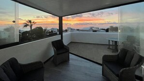 A modern balcony with two wicker chairs and a small table, overlooking a sunset with buildings in the distance. - Tranquil setting, sea view, heated pool & Hot Tub, sub-tropical garden. (Playa Blanca)
