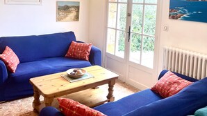 Ein Wohnzimmer mit einem blauen Sofa, einem Holztisch und einem großen Fenster mit Blick auf Grünflächen.