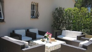 Eine Terrasse im Freien mit Korbmöbeln, einem Tisch mit floraler Dekoration und einem an der Wand befestigten abstrakten Kunstwerk.