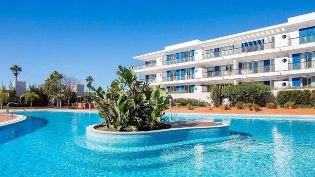 A modern hotel with a pool, surrounded by tropical plants and palm trees. - Marina de Lagos Apartment  (Lagos)