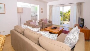 A living room with a sofa set, a coffee table, a TV stand, and a balcony with a view. - Marina de Lagos Apartment  (Lagos)