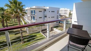 A balcony with a view of modern buildings, a palm tree, and a table with chairs. - Marina de Lagos Apartment  (Lagos)