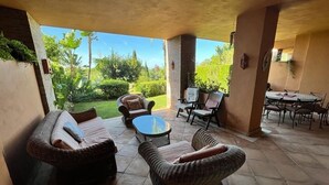 Un espace extérieur aménagé en terrasse, avec des meubles en osier, une table en verre et une vue sur un jardin luxuriant.