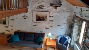 Une pièce chaleureuse avec un mur en pierre, un tableau encadré, un canapé, un fauteuil et une table avec une lampe.