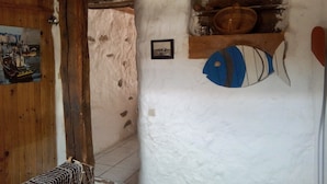Une pièce rustique avec une porte en bois, un mur blanc orné d’un motif de poisson, une petite étagère avec un panier et un tableau encadré.