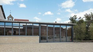 A modern building with a large glass facade, a stone base, and a bell tower in the background. - House / Villa - St rémy le petit (Saint-Remy-Le-Petit)
