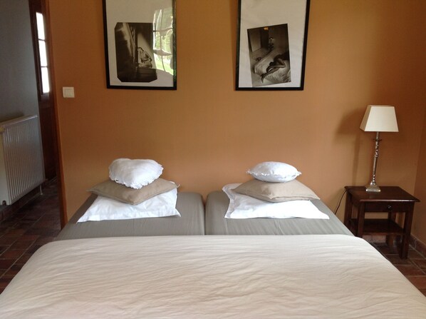 A hotel room with two beds, each with a pillow and a blanket. There is a small table with a lamp, and two framed pictures on the wall. - House / Villa - VILLENY (Villeny)